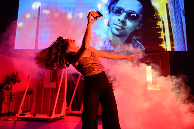 THE VILLAGE: a performer in red light in front of a live video feed